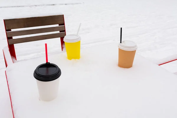 Three cups of coffee are on a snow-covered table in a winter park.