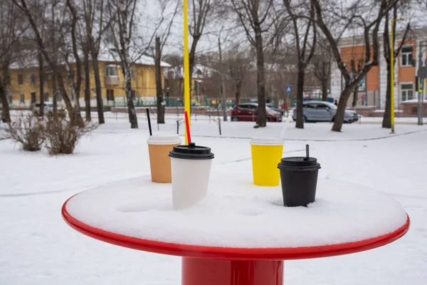 Four cups of coffee are on a snow-covered table in a winter park.
