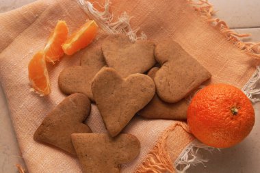 Kalp şeklinde ev yapımı zencefilli kurabiyeler, mandalinalarla birlikte, peçetenin üzerinde yatar..