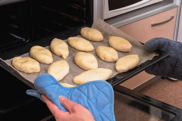 A woman puts Russian pies made of raw dough with filling into the oven for baking. Homemade baking.