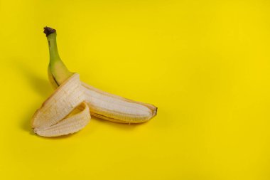 Sarı zemin üzerinde olgun ve lezzetli posası olan yarım soyulmuş bir muz. Reklam kavramı.