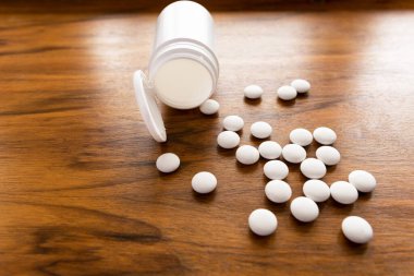 Masanın üzerinde beyaz haplar ve boş beyaz bir şişe var..