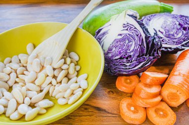 Kasede pişmiş beyaz fasulye, masada kırmızı lahana ve havuç parçaları var. Vejetaryen yemeği..