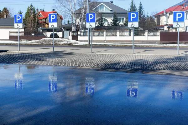 Krasnoyarsk, Rusya - Mart 06, 2021: Şehirdeki dört engelli park yeri özel işaretlerle işaretlendi. İşaretler su birikintisine yansıyor..