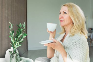 Sabahları mutlu, orta yaşlı bir sarışın kahve ya da çay içer, elinde bir bardak tutar..