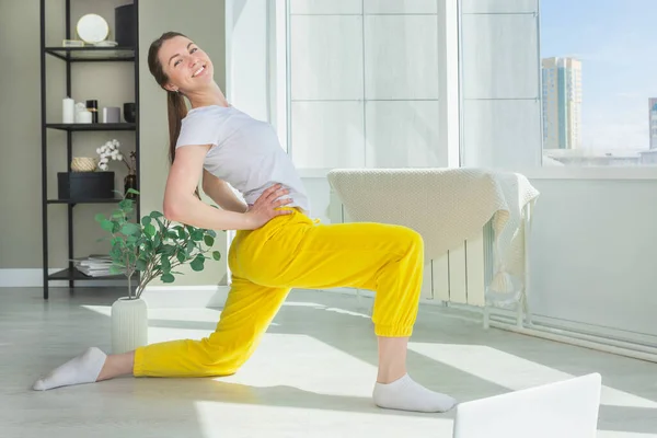 İnternette pilates yapan genç bir kadın. Kız sabah egzersizleri yapıyor. Çevrimiçi fitness atölyesi kavramı.