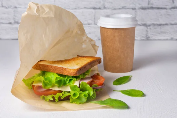 Peynirli sandviç, jambon ve salata, kağıt bardakta kahve. Yemek teslimatı konsepti, ofiste öğle yemeği.