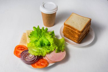 Sebze, peynir, jambon ve ekmek sandviçler için hazırlanır. Masanın üzerinde bir fincan kahve var. Fast food konsepti.