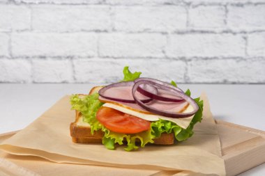 Kağıdın üzerinde marullu, domatesli, jambonlu ve peynirli bir sandviç var. Ofis yemekleri konsepti.