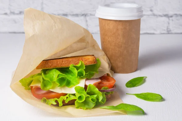 Peynirli sandviç, jambon ve salata, kağıt bardakta kahve. Yemek teslimatı konsepti, ofiste öğle yemeği.