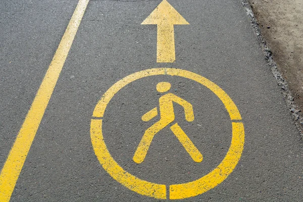 Yellow sign denoting pedestrian space on the road. Walking road in the park. Pedestrian figurine sign painted in yellow paint on black asphalt sidewalk.