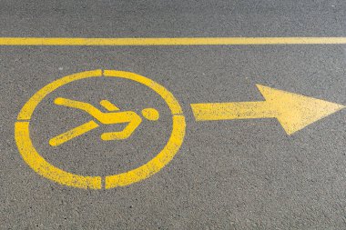 Yoldaki yaya alanını gösteren sarı tabela var. Parkta yürüyüş yolu. Siyah asfalt kaldırıma sarı boyayla boyanmış yaya ait biblo tabelaları..