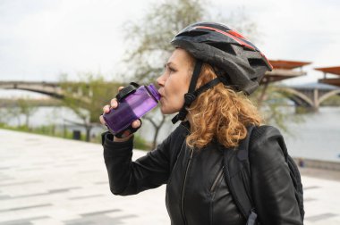 Bisiklet kasklı bir kadın bisiklet sürdükten sonra su içer. Sporcu kadın şişeden su içiyor..