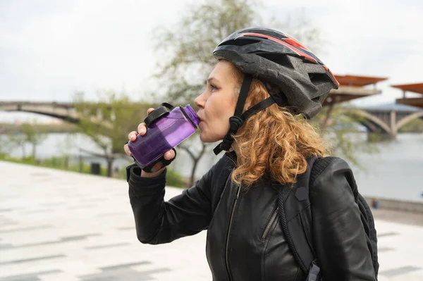 Bisiklet kasklı bir kadın bisiklet sürdükten sonra su içer. Sporcu kadın şişeden su içiyor..