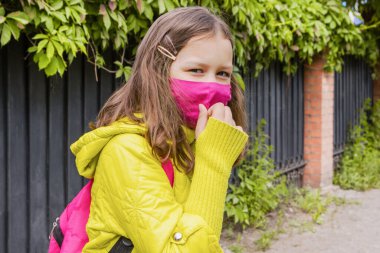 Pembe çantalı, sarı ceketli ve pembe maskeli 9 yaşında bir kız okula gidiyor. Çocuklar için kurslar Eylül ayında başlıyor.