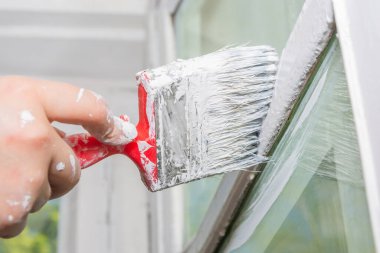 Pencere tamiri yapan bir kadın. Bir kadın eski ahşap bir pencere çerçevesini beyaz boyayla boyuyor..