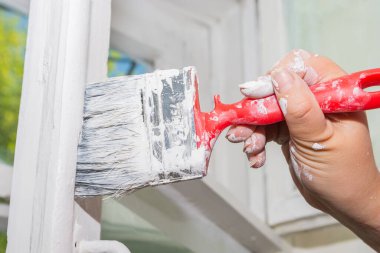 Pencere tamiri yapan bir kadın. Bir kadın eski ahşap bir pencere çerçevesini beyaz boyayla boyuyor..