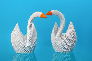 Mavi arka planda kırmızı gagalı iki beyaz origami kuğusu..