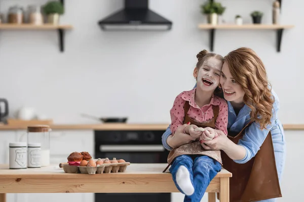 Anne ve kızı mutfak masasında oturmuş gülüyorlar.