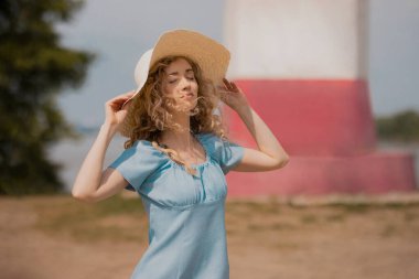 Mavi elbiseli ve büyük hasır şapkalı kız güneşin tadını çıkarıyor.