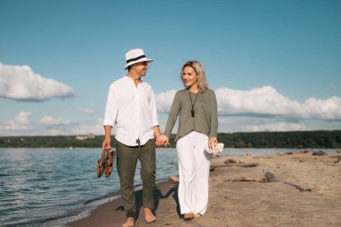 Kadın ve erkek güneşli havada sahilde yürür.