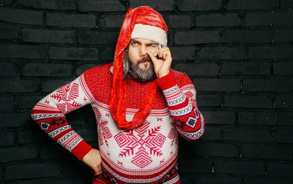 Kırmızı kazaklı, kırmızı şapkalı, siyah sakallı, siyah tuğlalı duvarlı genç Noel Baba.