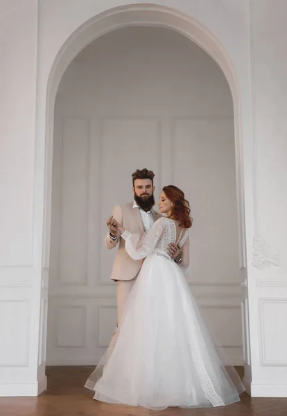 Beyaz elbiseli bir adam ve bir kadın beyaz bir duvara yaslanır ve bir düğün dansı yapar.