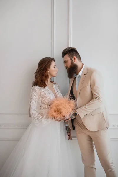 Beyaz elbiseli bir adam ve bir kız beyaz bir duvarın önünde duruyorlar.