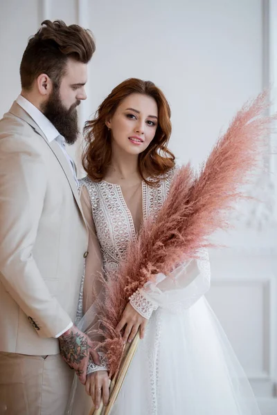 Beyaz elbiseli bir adam ve bir kız beyaz bir duvarın önünde duruyorlar.