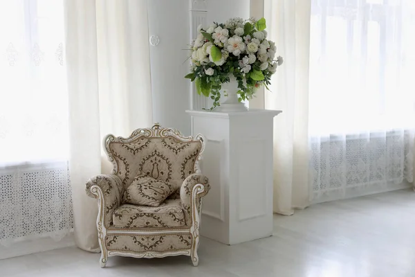 a beige ornamented armchair stands in a bright room