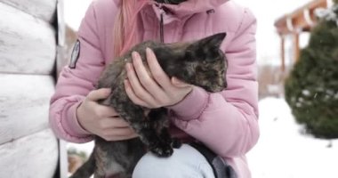 Üç renkli bir kedi yavrusu kışın açık havada bir kızın kollarında oturur.