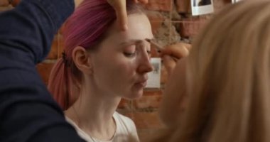 Bir kadının yüzü, çatı katı tarzı bir odada makyaj sanatçısı tarafından boyanır.