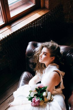 Hassas beyaz gecelikli güzel bir kadın kahverengi bir kanepede yatıyor.