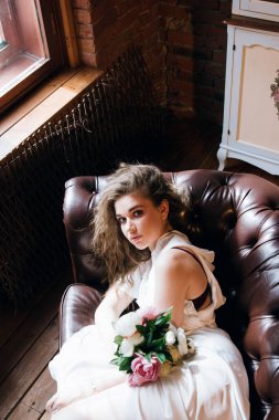 Hassas beyaz gecelikli güzel bir kadın kahverengi bir kanepede yatıyor.