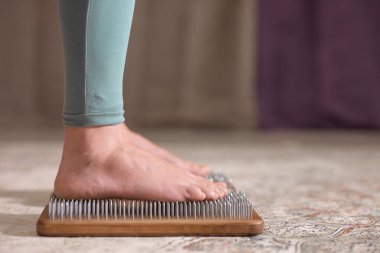 Yogi kadın çivilerin üzerinde duruyor, bacakları kapalı.