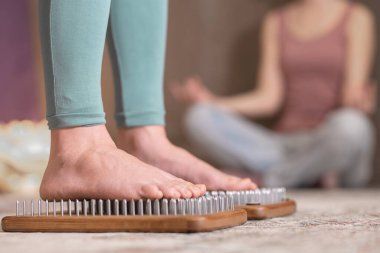 Yogi kadın çivilerin üzerinde duruyor, bacakları kapalı.
