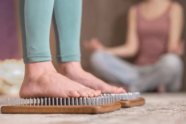 Yogi kadın çivilerin üzerinde duruyor, bacakları kapalı.