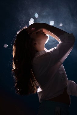 Genç bir kadın, parlak bir ışığın önünde, sabun köpüğü ve duman püskürtüsünün içinde.