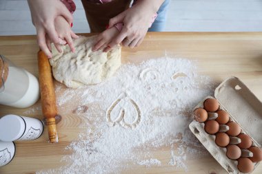 Anne ve kızı mutfakta un ile yemek hazırlıyor ve unun üzerine kalpler çiziyor.