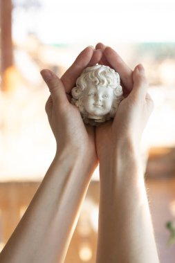 Bir kadın, elinde kırık bir melek heykeli, başını tutuyor.