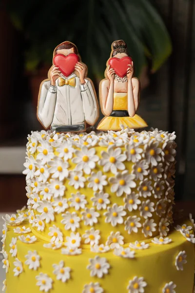 beautiful festive yellow cake with decorative man and woman who cover their faces with hearts