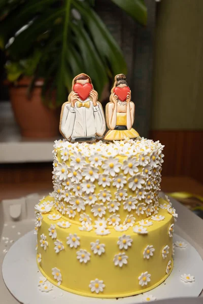 beautiful festive yellow cake with decorative man and woman who cover their faces with hearts