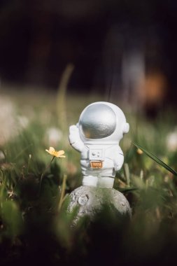 Oyuncak bir astronot uzun otların arasında duruyor ve elini sallıyor.