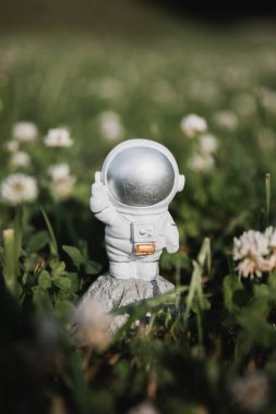 Oyuncak bir astronot uzun otların arasında duruyor ve elini sallıyor.