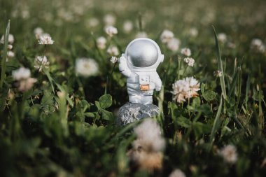 Oyuncak bir astronot uzun otların arasında duruyor ve elini sallıyor.