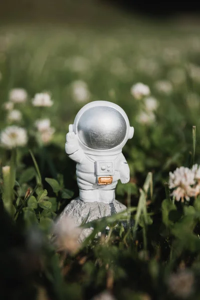 Oyuncak bir astronot uzun otların arasında duruyor ve elini sallıyor.