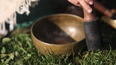 Bir kadın şarkı söyleyen bir Tibet kasesinin üzerinden ahşap bir deste sürüyor.
