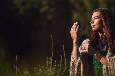 Yogi kadın ormanda oturuyor ve elinde sigara çubuğu tutuyor.