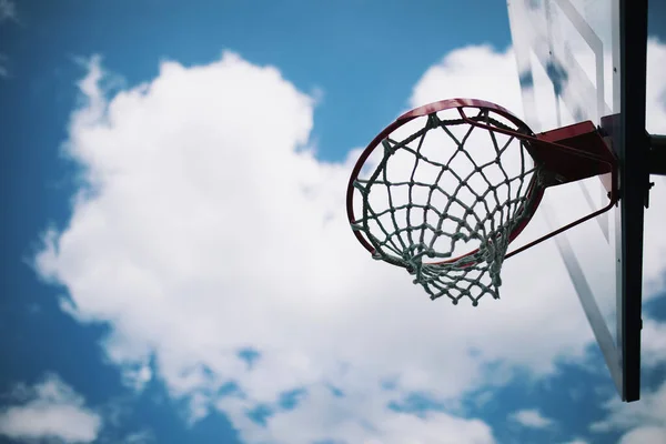 Mavi gökyüzü ve beyaz bulutların altında ağ ile basketbol potası