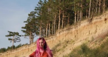 Pembe saçlı kadın güneşin ve kumsalda rüzgarın tadını çıkarıyor.